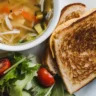 A bowl of chicken noodle soup served with a side of grilled cheese sandwich